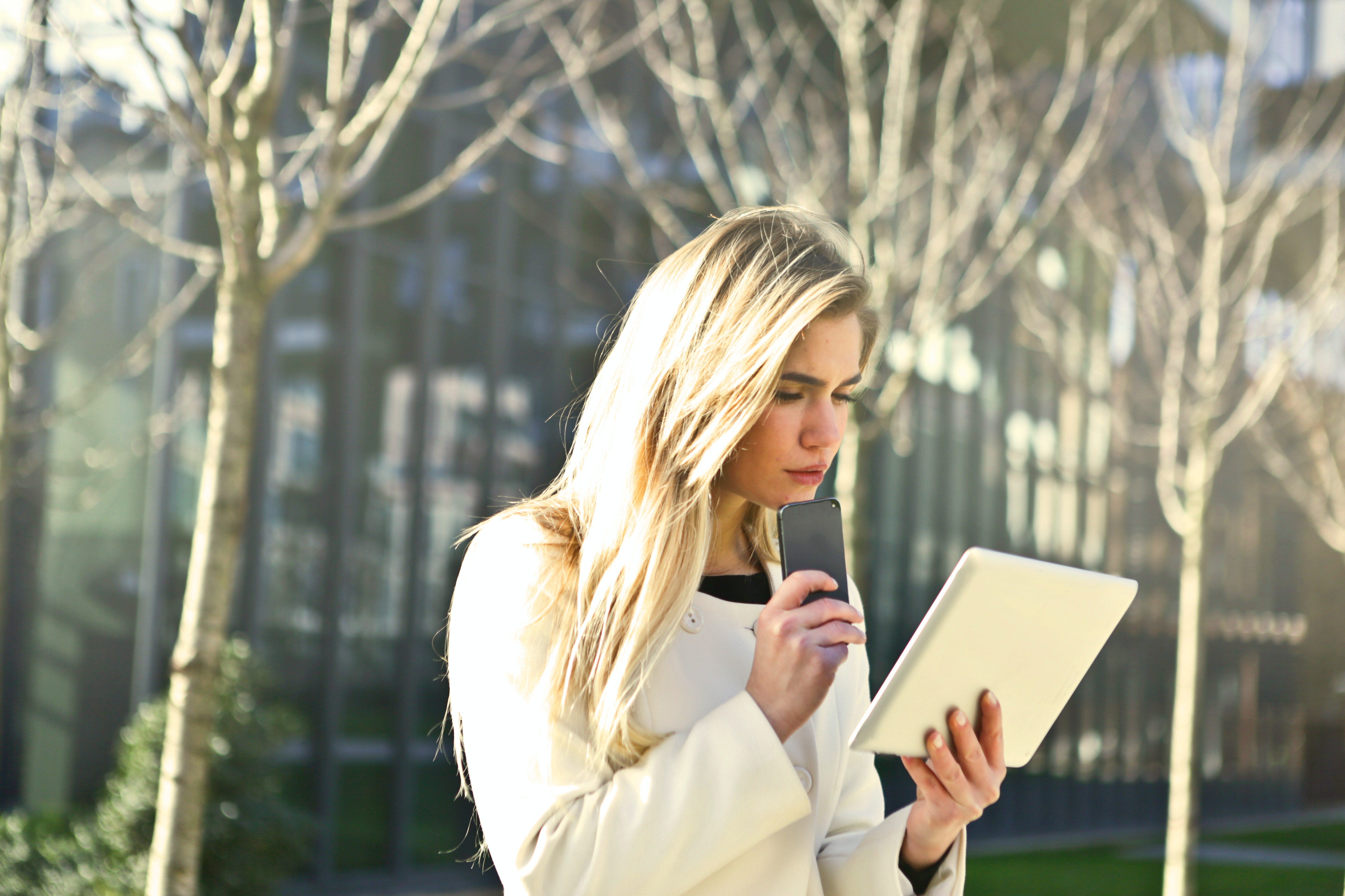 Kvinde står med en telefon i hånden og kigger undrende på en tablet.